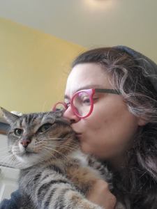 Photograph of Dollissa kissing an unwilling Haircut the Tabby Cat on her little fuzzy cheek. Haircut is displeased.