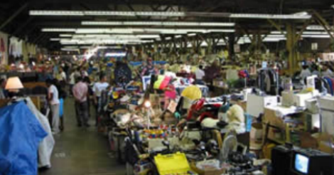A very low res blurry photo of the inside of a flea market. Trash is piled high.