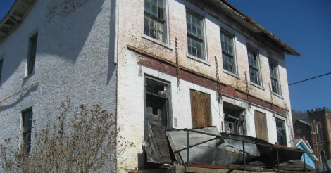 Photo of a once-grand old house. Its porch roof has fallen. Some windows are busted in. It needs paint -- and probably new floors... It looks like it's been vacant for 40 years.